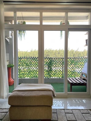 Quarto com uma grande porta de vidro deslizante que dá para uma varanda com vista para uma cerca verde e árvores.