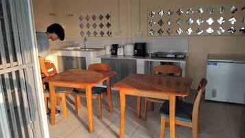 Una cocina compacta con comedor, que incluye un refrigerador, estufa, cafetera y una lámpara fijada a la pared.