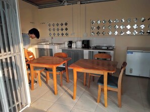 A compact kitchen with a dining area, featuring a refrigerator, stove, coffee maker, and a wall-mounted light fixture.