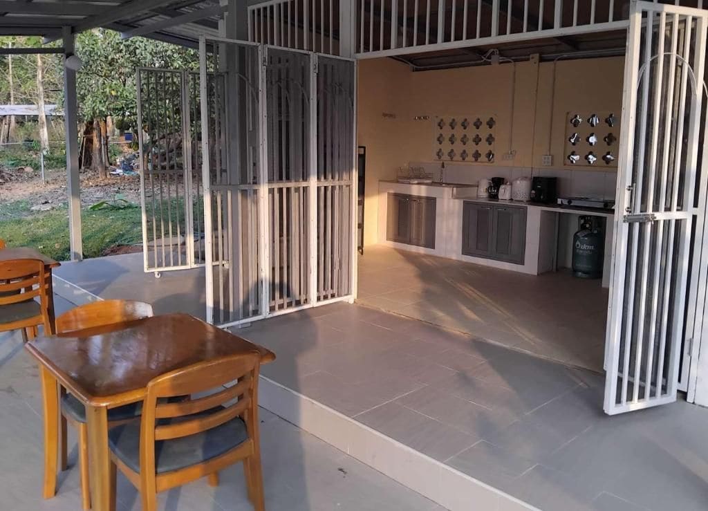 A covered outdoor seating area with a table and chairs, a kitchen with cabinets and appliances, and a gated entrance.