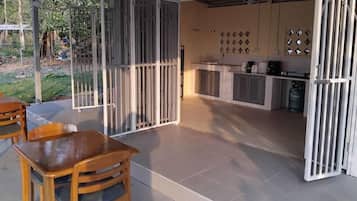 A covered outdoor seating area with a table and chairs, a kitchen with cabinets and appliances, and a gated entrance.
