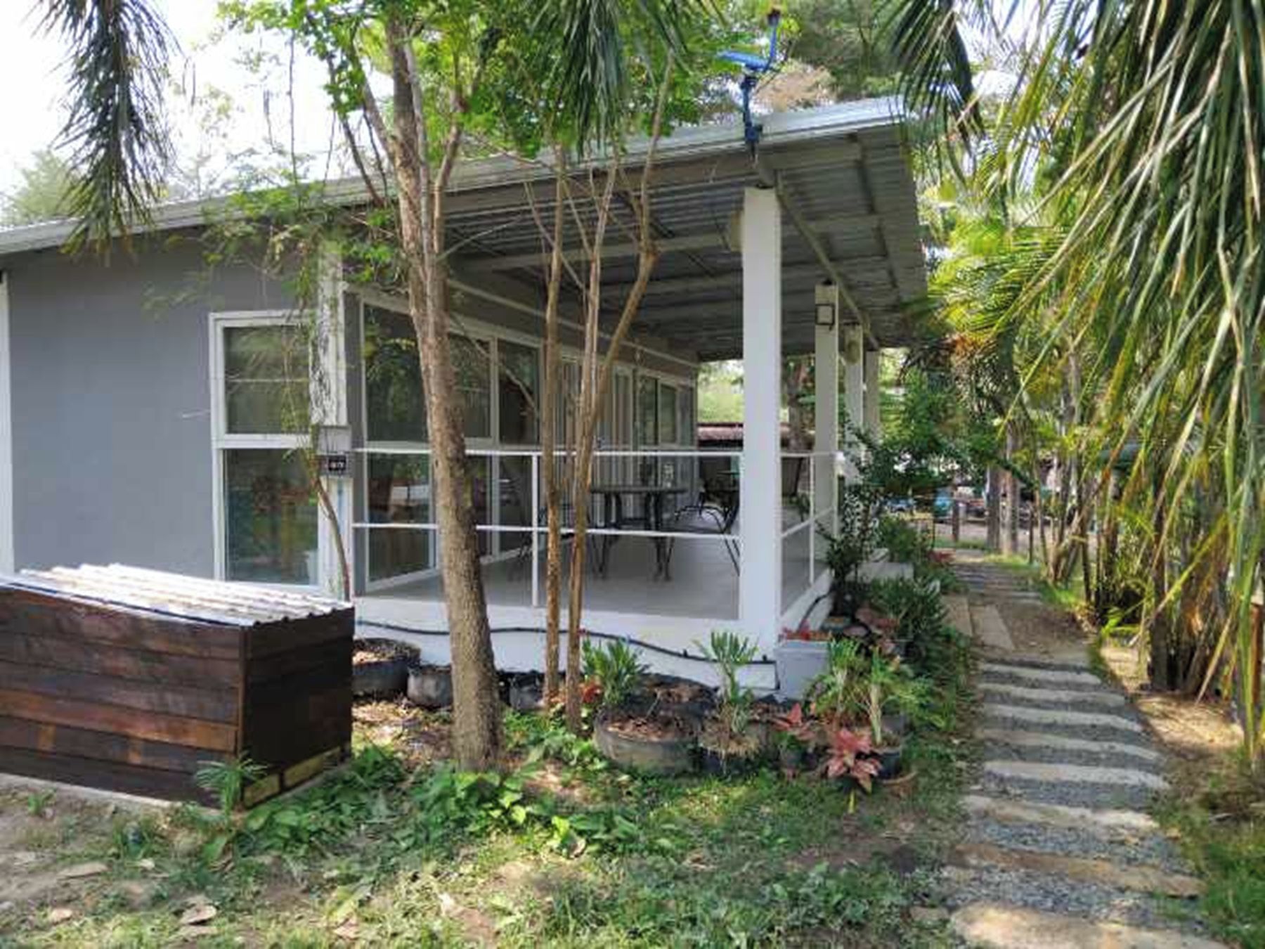 Une petite maison à un seul étage, dotée d’un porche abrité et entourée d’une végétation tropicale.