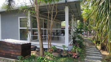 Une petite maison à un seul étage, dotée d’un porche abrité et entourée d’une végétation tropicale.
