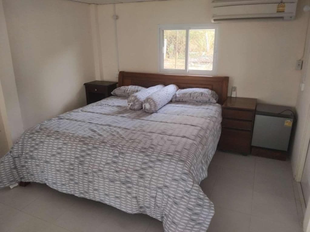 Een slaapkamer met een bed, nachtkastje, dressoir en raam.