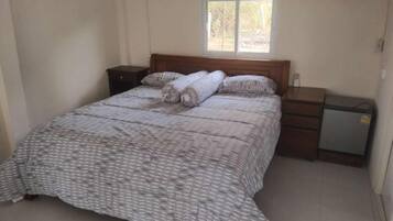 Een slaapkamer met een bed, nachtkastje, dressoir en raam.