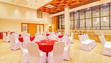 Un salón de banquetes con mesas redondas, sillas blancas y manteles rojos.