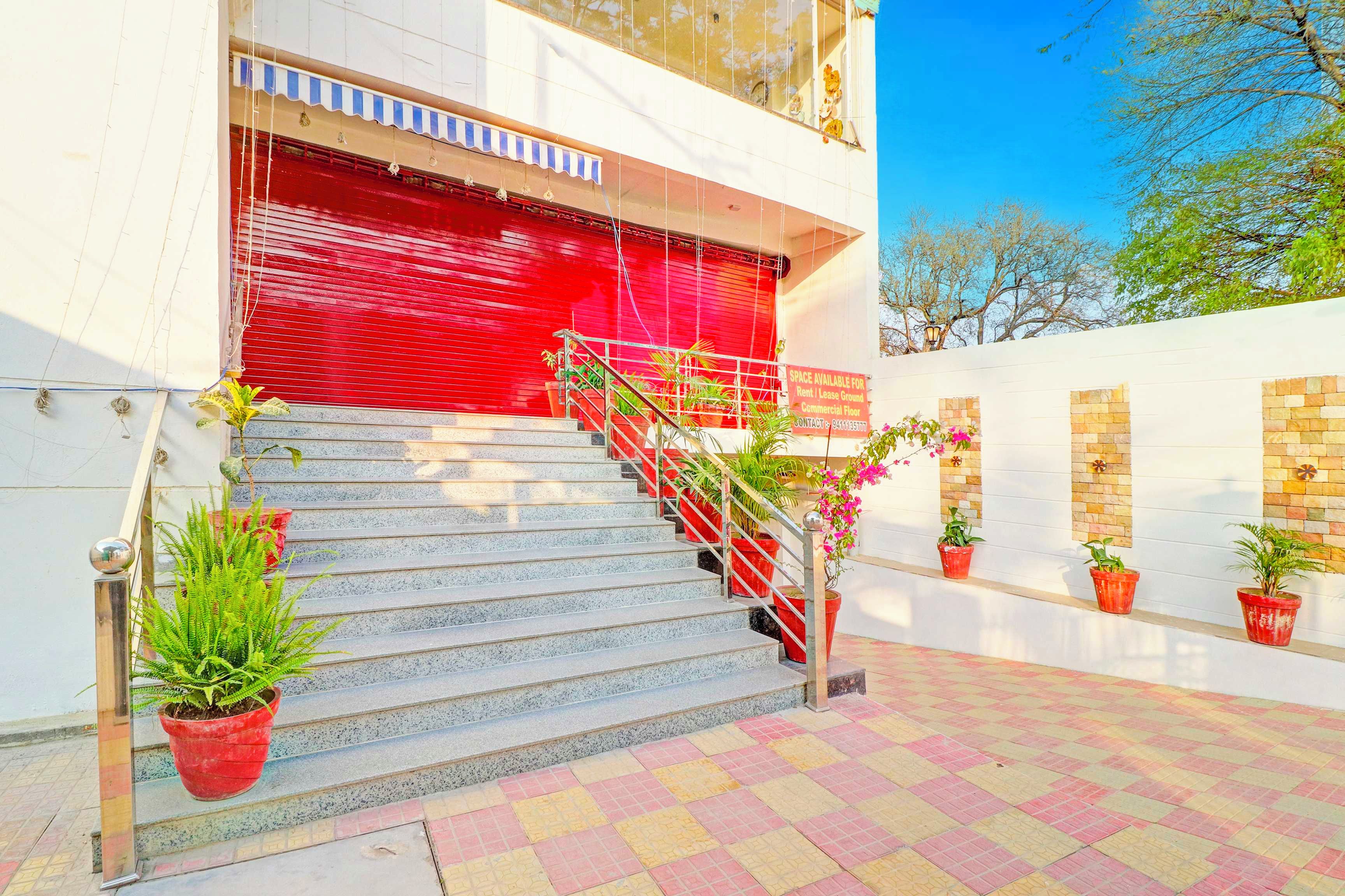 Una entrada de edificio con un persiano rojo, una escalera y plantas en macetas.