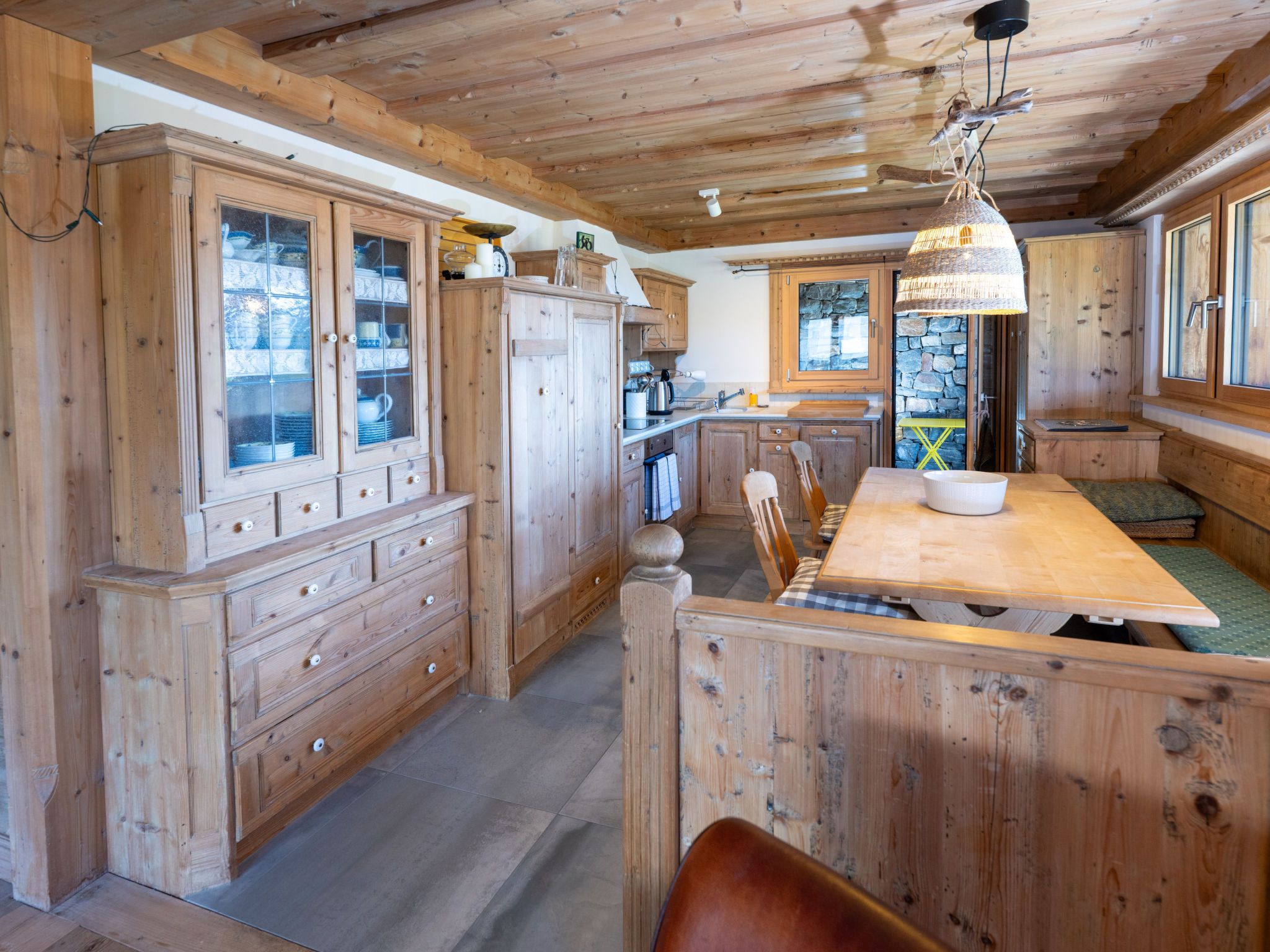 Un intérieur en bois avec une table à manger centrale, des meubles de rangement en bois et un mur en pierre.