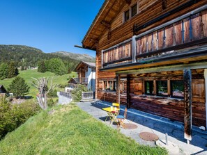 Eine Holzchalet mit Balkon, einem Steinweg und Blick auf die umliegende Landschaft.