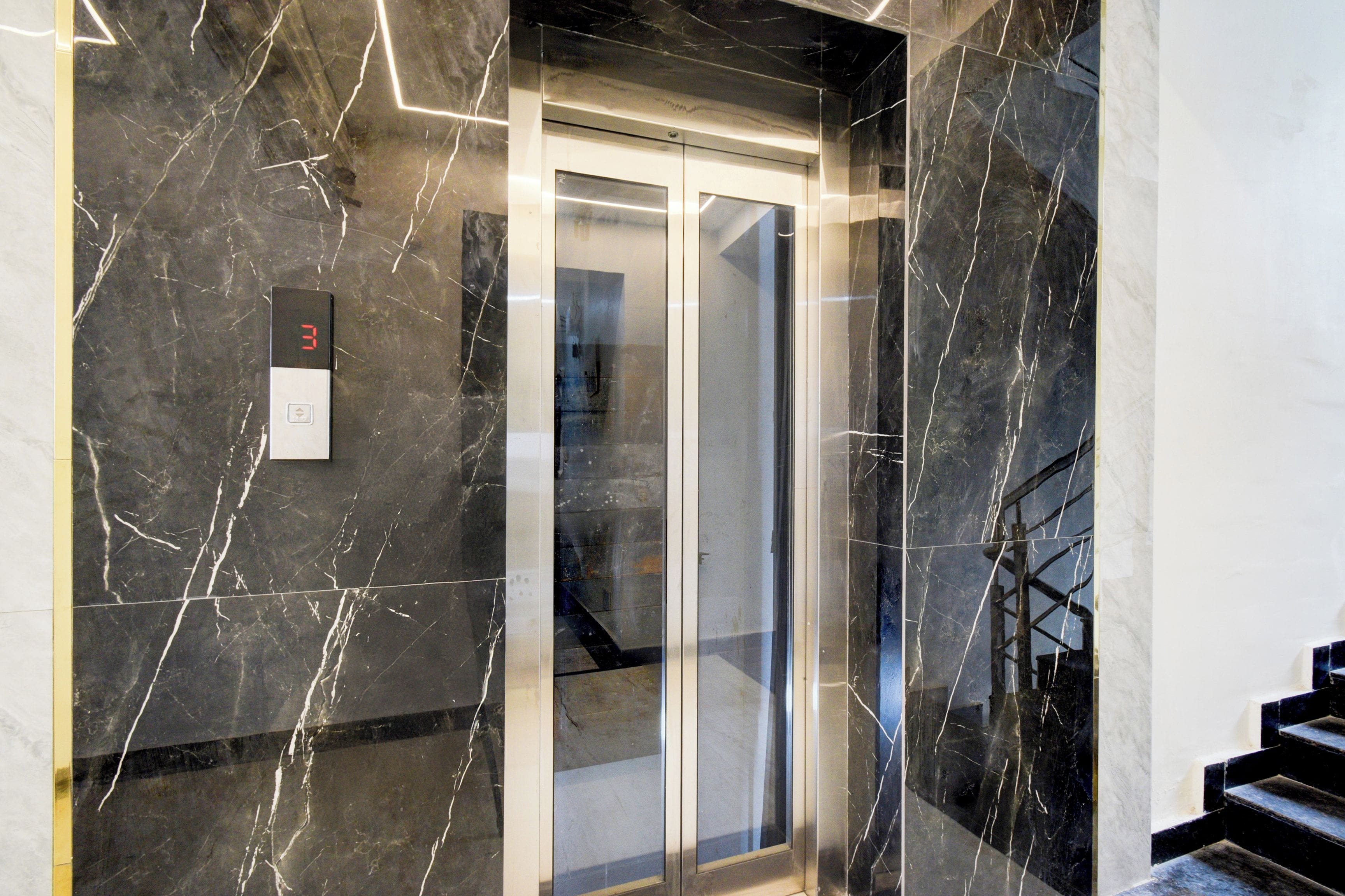 A modern elevator with a digital display, marble walls, and a staircase.