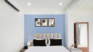 Quarto de hotel com cama, mesa de cabeceira, luminária e ar-condicionado fixado na parede.