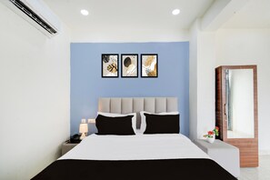 A hotel room with a bed, bedside table, lamp, and a wall-mounted air conditioner. - Townhouse Nagole Metro Station (Hyderabad)