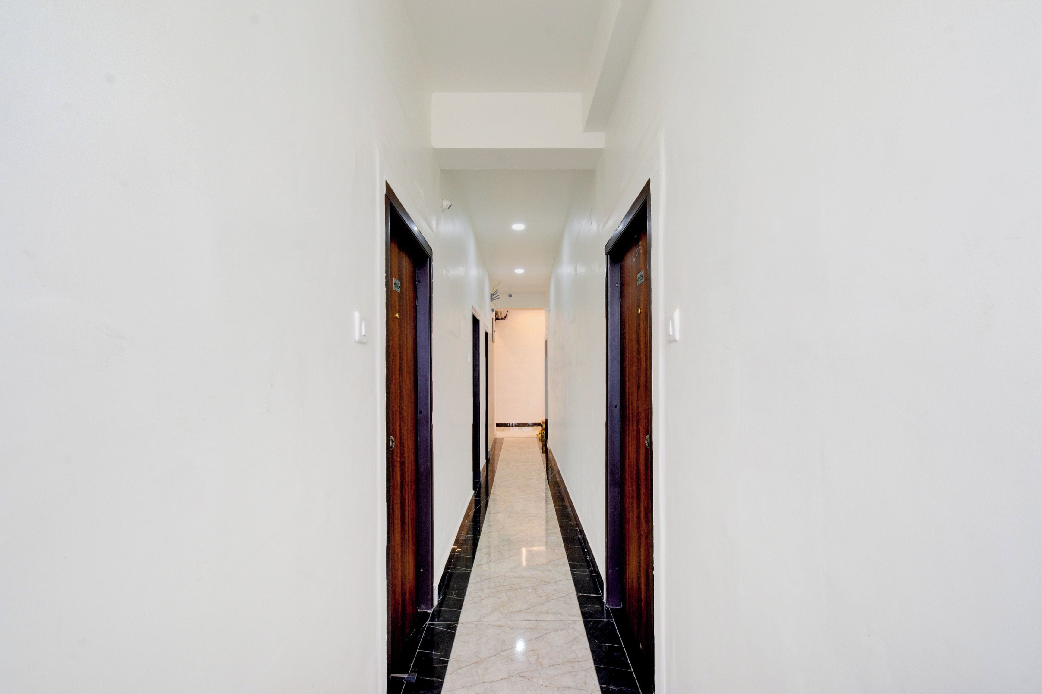 A corridor with doors on both sides, a tiled floor, and a ceiling with recessed lighting.