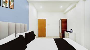 Habitación de hotel con una cama, una puerta de madera, un escritorio blanco con cafetera y cuadros en la pared.
