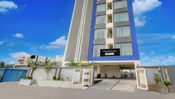 Uma casa geminada moderna com entrada destacada, placa visível indicando serviço OYO e céu azul claro ao fundo.