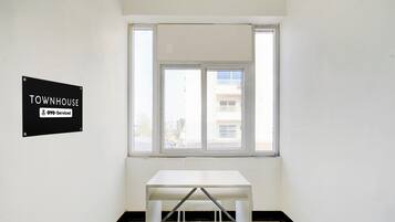 Een kamer met een witte tafel en een raam. Op de muur hangt een bordje met de tekst 'TOWNHOUSE OYO-Serviced'.