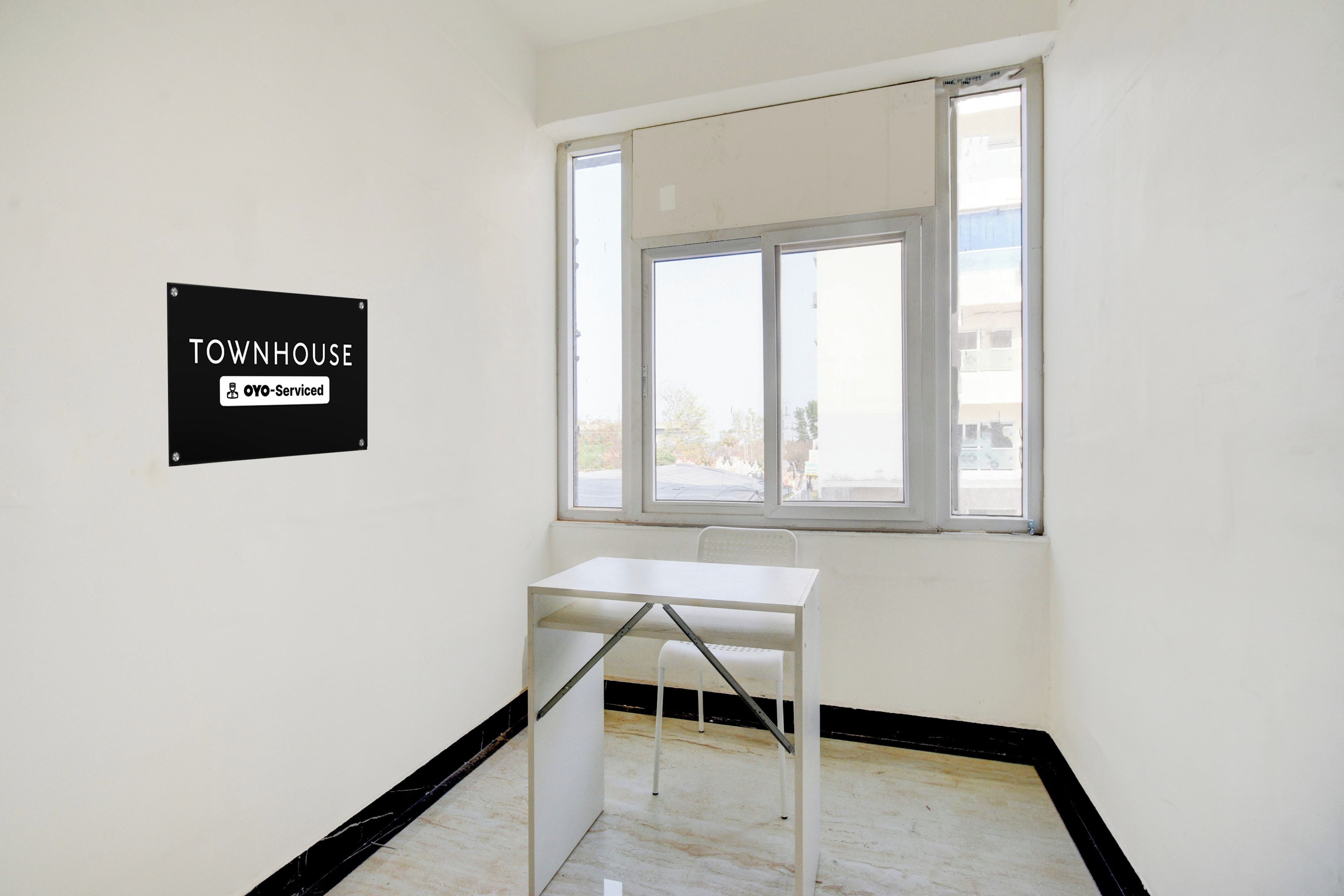 A room with a white table and a window, a sign on the wall, and a view outside.