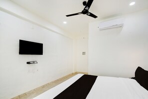 Quarto de hotel com cama, TV de tela plana na parede, ventilador de teto e ar condicionado.