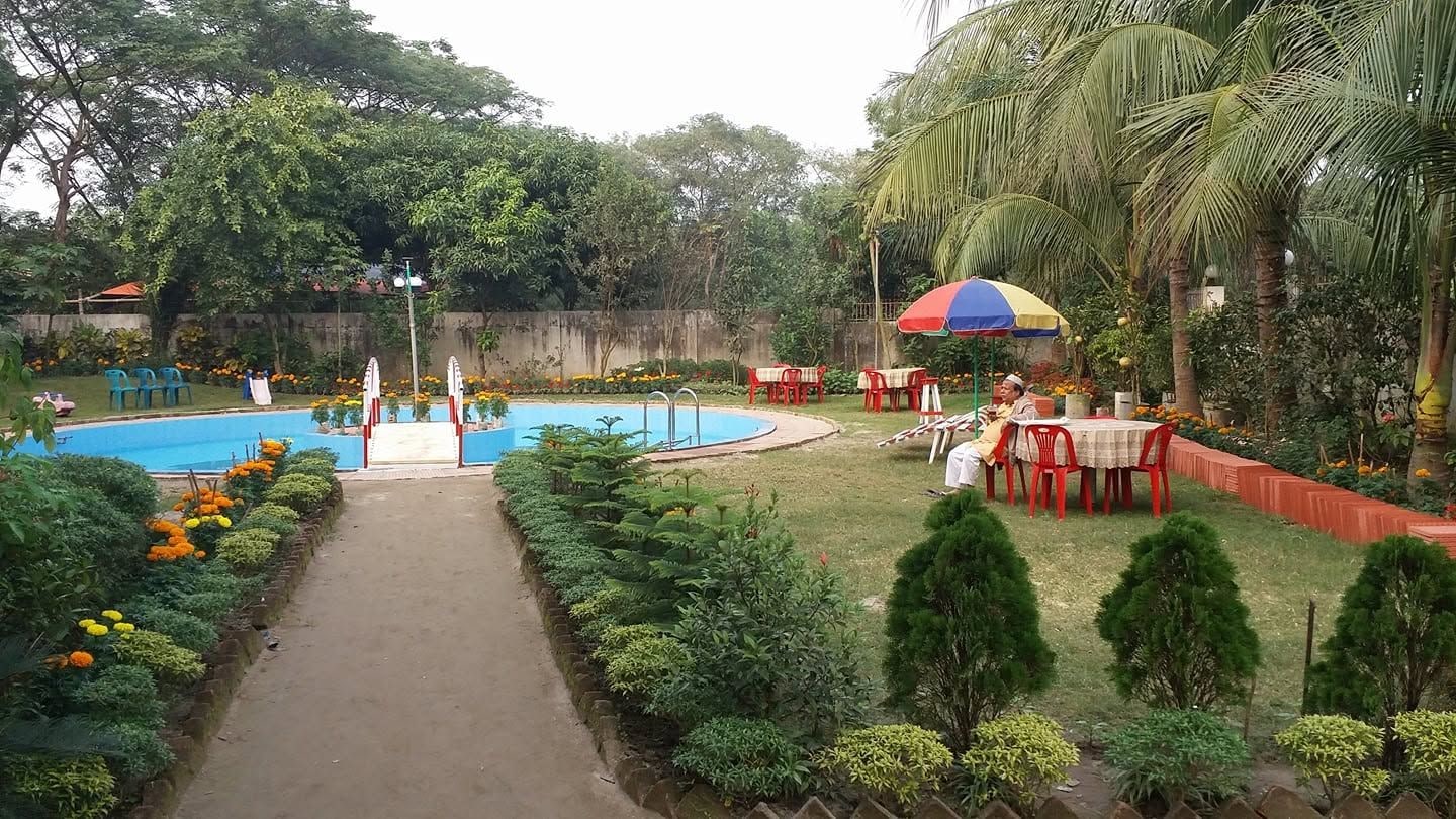 Zona de piscina con un camino, asientos y una persona bajo un paraguas colorido.