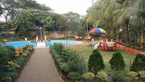 A pool area with a pathway, seating, and a person under a colorful umbrella.