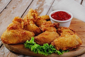 Pechugas de pollo frito sobre una tabla de madera con lechuga y un tazón pequeño de kétchup.