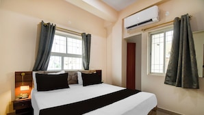 A hotel room with a bed, a nightstand, an air conditioning unit, and a window with curtains. - Super Townhouse Kumhrar Archeological (Patna)
