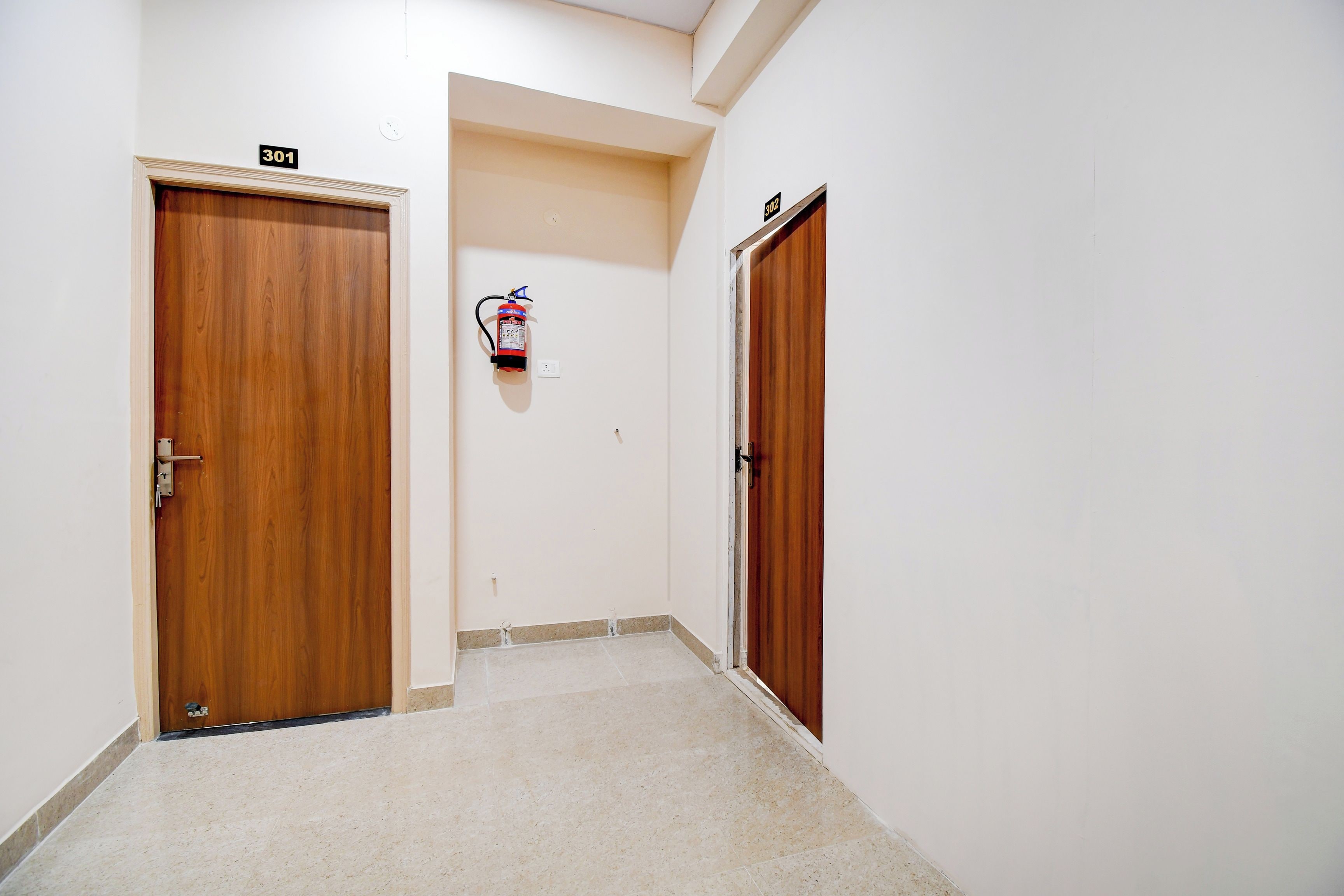 Un pasillo con dos puertas de madera, cada una con un número, y un extintor colgado en la pared.