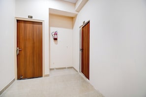 Un pasillo con dos puertas de madera, cada una con un número, y un extintor colgado en la pared.