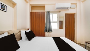 A hotel room with a bed, a wardrobe, an air conditioning unit, and a window with curtains. - Super Townhouse Kumhrar Archeological (Patna)