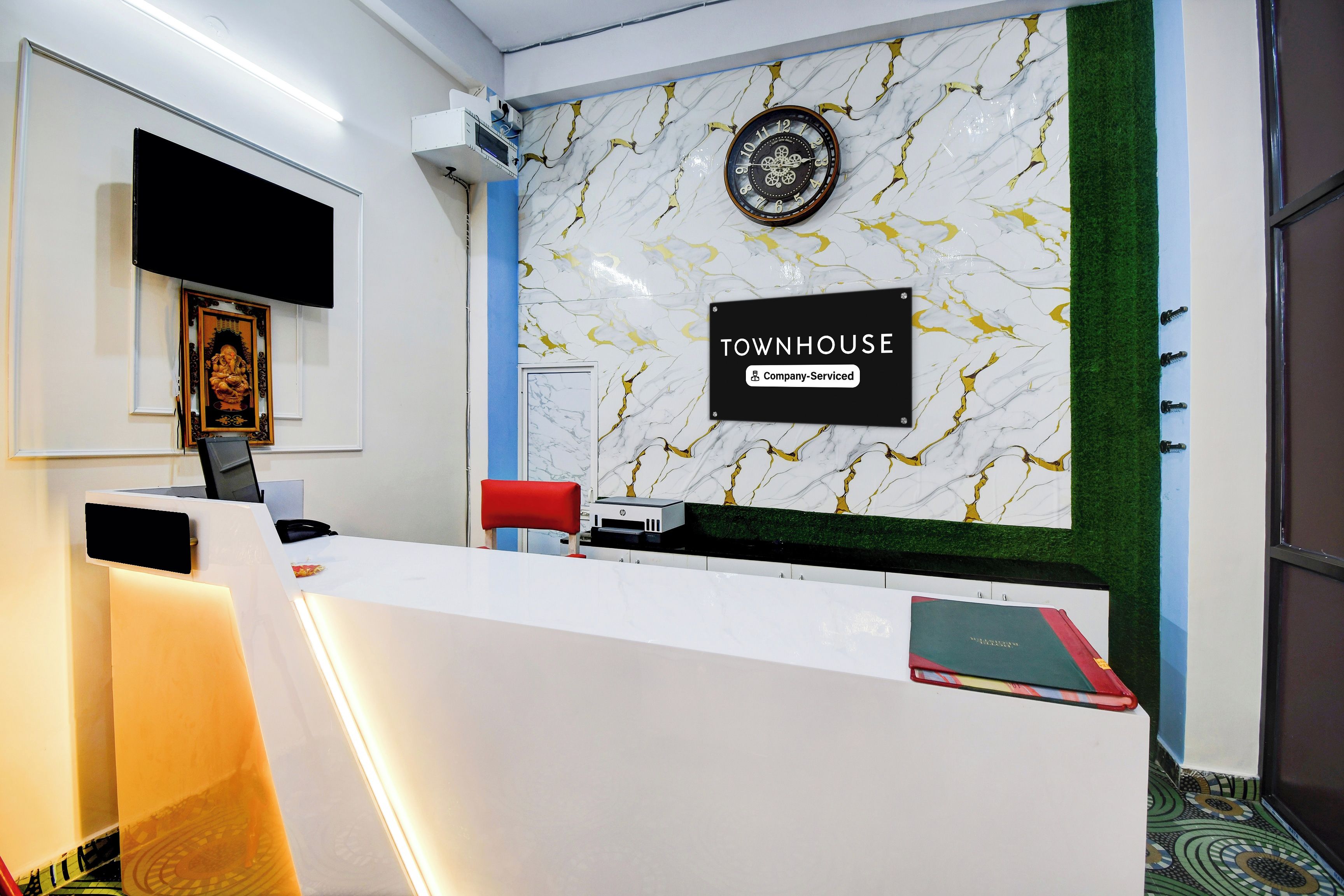 Una reception con una sveglia, una segnaletica che indica 'TOWNHOUSE Company-Serviced' e un quadro appeso al muro.