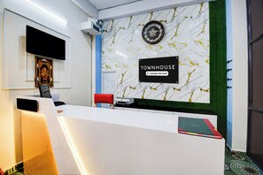 Un mostrador de recepción con un reloj, un letrero que indica 'TOWNHOUSE Company-Serviced' y un cuadro enmarcado en la pared.