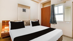 A hotel room with a bed, a bedside table with a phone, a mirror, and a window with curtains. - Super Townhouse Kumhrar Archeological (Patna)