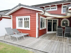 A red house with a covered patio, a sliding door, and a small deck with chairs. - Brandgans at Susanne-fischer Weg 43 (Wyk auf Foehr)