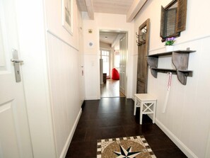 Ein Korridor mit dunklem Boden, weißen Wänden, einer kleinen weißen Bank und einem an der Wand befestigten Regal mit einer Pflanze.