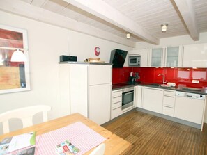 A kitchen with white cabinets, a red backsplash, a microwave, a coffee maker, and a wooden table with a placemat. - Brandgans at Susanne-fischer Weg 43 (Wyk auf Foehr)