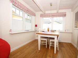 A room with a wooden floor, a white table with chairs, a window with blinds, and a red lamp on the wall. - Brandgans at Susanne-fischer Weg 43 (Wyk auf Foehr)