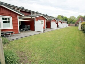 A row of red buildings with attached garages, a grassy yard, and outdoor seating. - Brandgans at Susanne-fischer Weg 43 (Wyk auf Foehr)