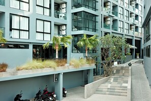 A modern building with multiple balconies, a covered walkway, and a few parked scooters. - Kamala - Beautiful Sunset Views (Kathu District)