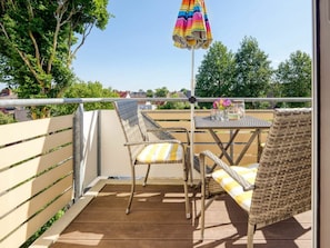 Ein Balkon mit Korbmöbeln, einem Tisch und einem bunten Sonnenschirm.