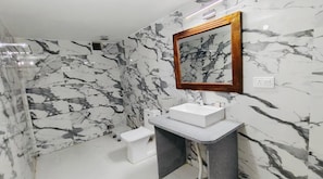 A bathroom with a marble wall, a wooden-framed mirror, a white sink, and a small white stool. - Jaisalmer Sand Dunes Luxury Camp and Resort (Jaisalmer)