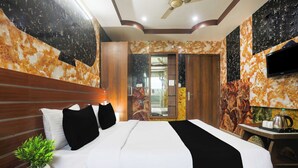 Una habitación de hotel con cama, televisión, escritorio con tetera y una planta.