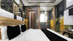 Habitación de hotel con una cama grande, cabecera de madera, mesita de noche con hervidor y vista al exterior por una ventana.