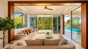 Un salón moderno con sofá, mesa de centro y un amplio ventanal con vistas a una piscina.