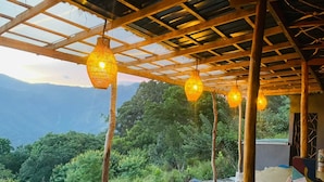 A covered outdoor seating area with hanging lights and a view of a mountainous landscape. - Dreamville (Ballaketuwa)