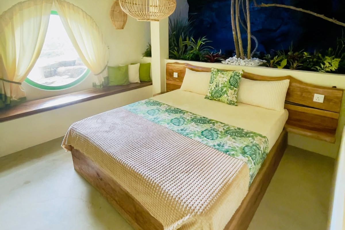 Une chambre à coucher avec un lit, un luminaire suspendu, une fenêtre avec des rideaux et une plante fixée au mur.