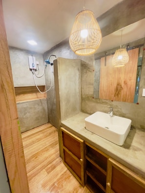 Une salle de bain avec un meuble-lavabo en bois, un lavabo blanc et une douche avec un flexible.
