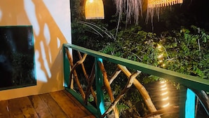 A wooden deck with a railing, a hanging light fixture, and a view of greenery. - Dreamville (Ballaketuwa)