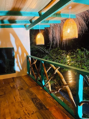 Une terrasse en bois avec une rambarde, un luminaire suspendu et une vue sur la verdure.