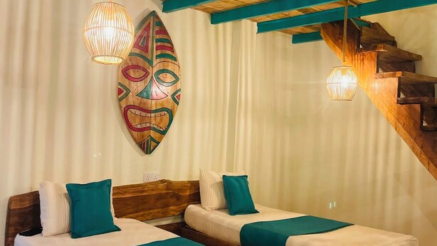 Quarto com duas camas de madeira, escada de madeira e máscara decorativa na parede.