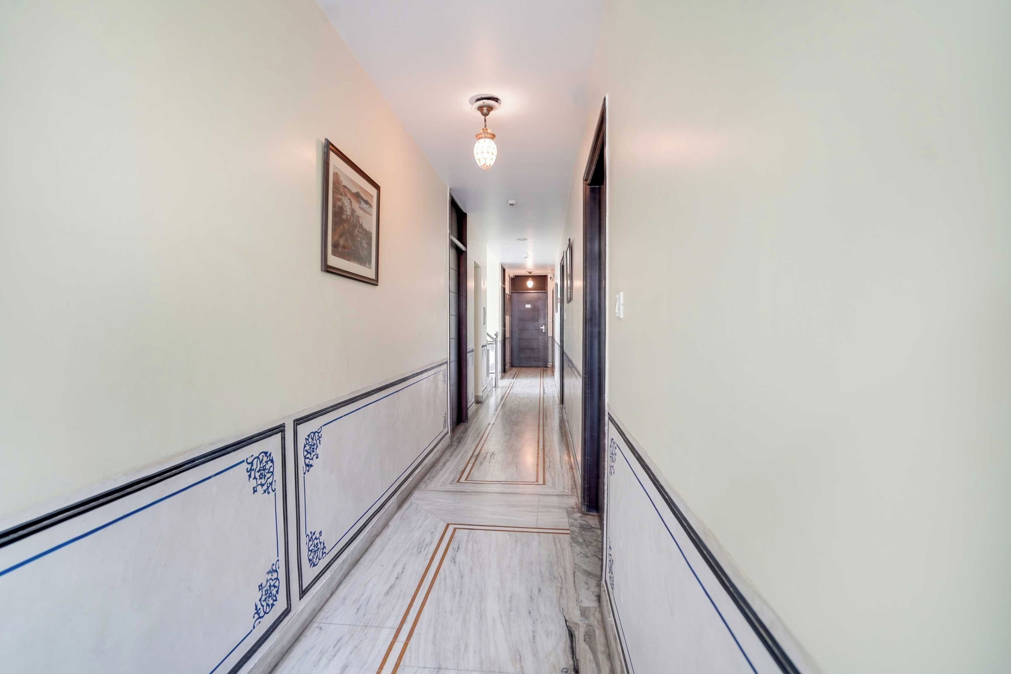 Um corredor com piso de mármore, obras de arte nas paredes e luminária no teto.